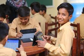 Pakistani rural students using tablets loaded with offline learning app while studying under a shaded school building.